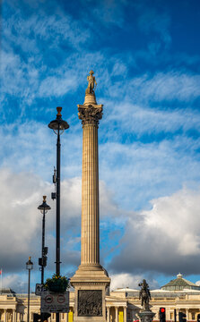 View of Nelson's Column with its statue of Admiral Nelson, ornate capital, and bronze reliefs under a blue sky with clouds in London, England, United Kingdom.