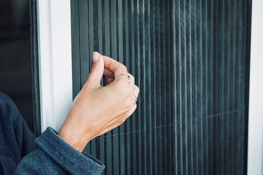 Close-up of a woman's hand touching a fine mesh screen door, highlighting durable insect protection, ventilation and quality household materials