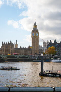 View of Big Ben and the Palace of Westminster rising above the River Thames with a bridge and cloudy sky in London, England, United Kingdom.