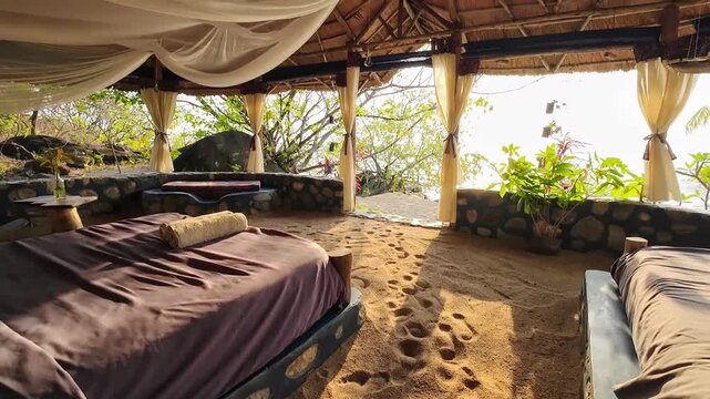 Sunrise pours into a unique open-air beach accommodation with a bed, sandy floor and curtains, offering an immersive stay surrounded by nature.