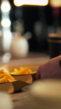 In an industrial kitchen, a male chef prepares portions of freshly cooked French fries, using a metal tool to serve the food onto paper plates. The concept of fast food in a street kitchen