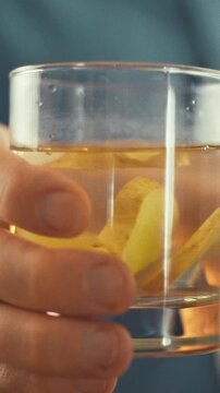 In a bright kitchen, a man extends a clear glass of ginger water, a beverage presented as part of a healthy food routine, as a morning hydration habit in a clean, functional setting