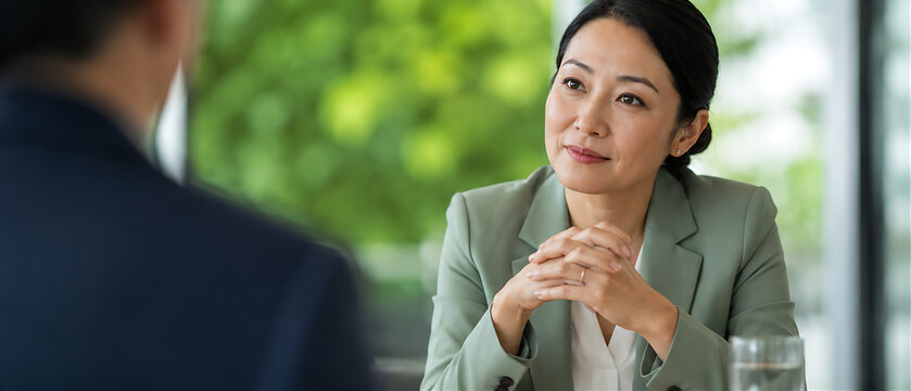 Intimate close-up of female leader showing empathy while listening &mdash; clasped hands, silver ring, sage blazer, plant wall bokeh, leadership

