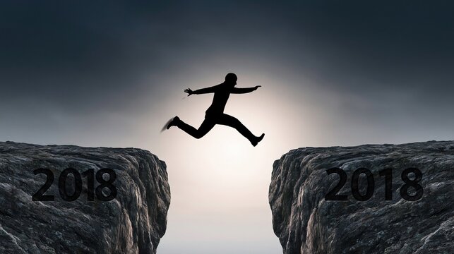 Silhouette of a businessman leaping across a chasm between two rocky cliffs marked with the year twenty eighteen against a dramatic sky