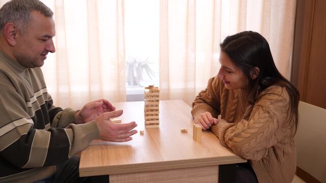 Players interact during a tabletop game, studying the tower and preparing for the next move with focused attention.