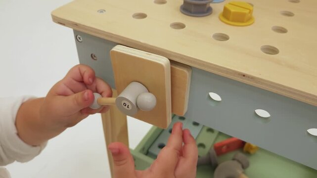 Child hands turning a wooden vice handle on a toy workbench in a brightly lit room. Toy manufacturing