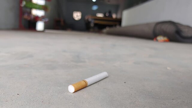 Single cigarette on concrete floor. Unused cigarette lies on ground. Concept of smoking habit.