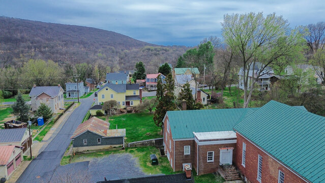 Bright green church roof borders Washington Street alongside historic brick houses. Sloping forested mountain ridges frame quiet residential enclave in Harpers Ferry, West Virginia