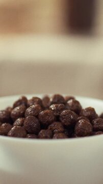 A white bowl of chocolate cereal rests on a wooden table bathed in morning light, creating a bright breakfast scene, the setting conveys a simple, healthy food arrangement in a cozy kitchen