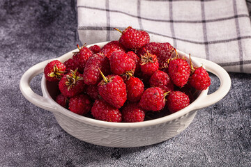 Fresh red raspberries in white ceramic bowl on textured gray surface with checkered cloth background © Andrei Starostin