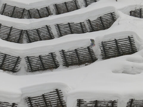 View of a snowboarder jumping over snow-covered avalanche fences in the mountains of Niseko, Hokkaido, Japan.