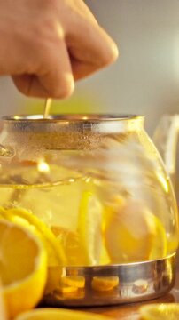 A man stirs a tea blend in a teapot, adding sliced lemon and ginger, creating a fragrant beverage as the mixture releases aroma, during the preparation process in a kitchen setting