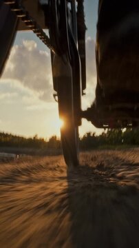 A cyclist rides a bicycle along a dirt path at golden hour, sunflowers line the route and warm sunset light illuminates the scene, reflecting daily outdoor recreation and cycling sport