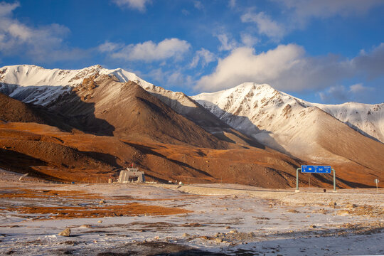 View of the Kunjirap Daban border crossing nestled among snow-capped mountains under a clear blue sky in Kashgar Prefecture, China.