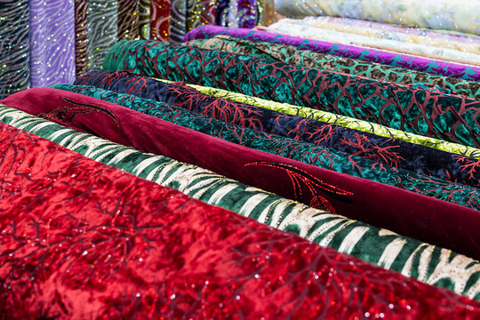 Colorful velvet and embroidered fabric rolls stacked at an oriental bazaar in Bukhara, Uzbekistan. Rich textures and vibrant patterns ideal for textile, fashion, and travel content.