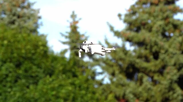 Drone hovers outdoors.
Aircraft crosses sky.
Propellers support flight.
Trees frame background.