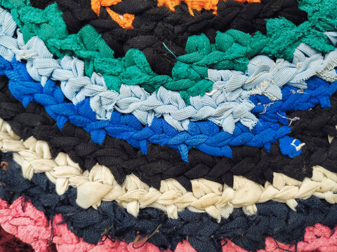 Close-up of a colorful handmade rug woven from many different strips of fabric. The background is a vintage antique floor covering with an abstract pattern.