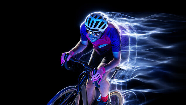Male cyclist races forward under bright electric energy waves on black background. Concept of cycling apparel, endurance training and race technology.