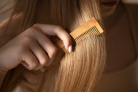 Female with long straight hair using a wooden comb to style her hair, soft lighting highlighting the texture and shine of the hair in a close-up view