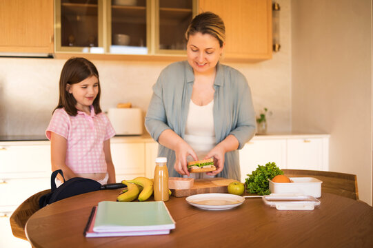 Woman and girl preparing healthy sandwich together in modern kitchen with fresh fruits and vegetables on wooden table, bright and inviting atmosphere