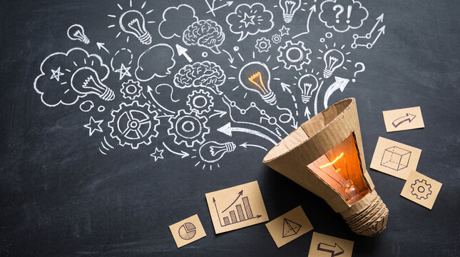 Cardboard lightbulb with glowing filament, surrounded by chalk drawings of ideas, gears, and graphs, symbolizing creativity and innovation