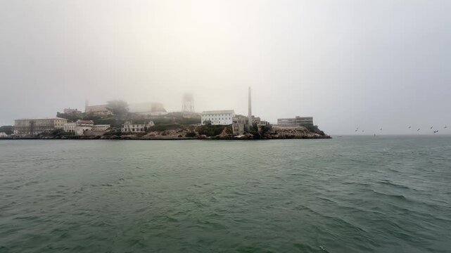 riding across San Francisco Bay, California, near the Golden Gate strait on a foggy day, while passing by Alcatraz Island with buildings of famous United States Penitentiary, partly covered with fog