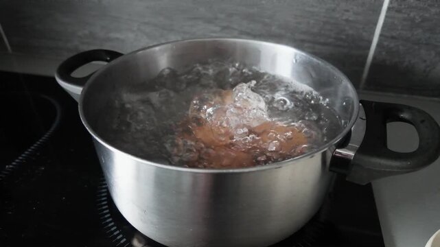 Eggs boiling in bubbling water inside a stainless steel pot