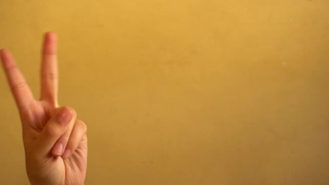 4K footage of a human hand making a peace sign against a simple background. Making it suitable for content about communication, gestures, positivity, friendship, peace, and everyday expressions.