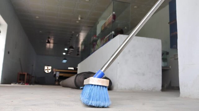 Blue cleaning broom on a dusty concrete floor. Close up of a long handle brush sweeper in an empty commercial building interior.