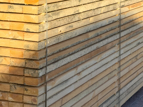 Stacked wooden lumber planks and timber boards neatly arranged on paved ground. Construction material, carpentry, lumberyard industry, and raw material storage detail.