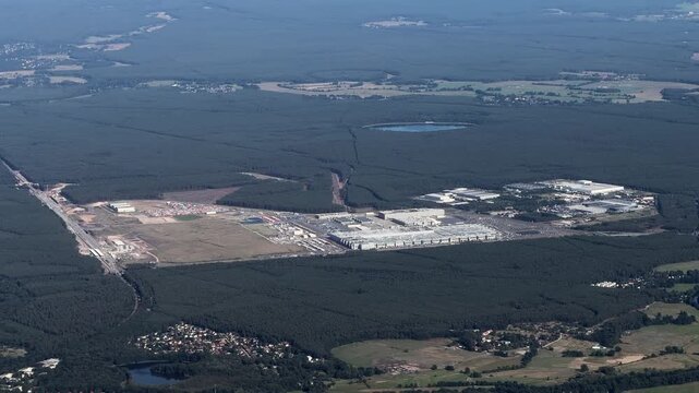 flying along Tesla Gigafactory 4, a manufacturing plant for Tesla Inc located southeast of central Berlin, in Brandenburg, GER, surrounded by forest and countryside landscape - 4k aerial video footage