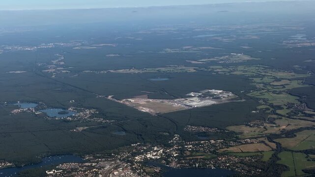 panoramic aerial view - flying along area around Tesla Gigafactory 4, a manufacturing plant for Tesla Inc. located southeast of central Berlin, in Brandenburg, Germany, surrounded by countryside