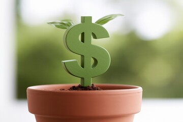 Fototapeta premium Green dollar symbol sprouting from soil in a terracotta pot with small leaves against a blurred natural background