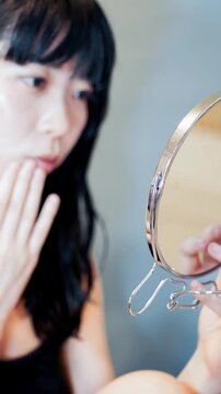手鏡を見ながら肌トラブルや口元を気にする女性_縦長