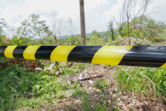 Yellow and black striped warning tape stretched across dense green vegetation to restrict entrance to a dangerous zone or property. Ideal for security presentations, environmental crime articles, safe