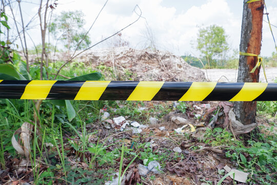 Yellow and black striped warning tape stretched across dense green vegetation to restrict entrance to a dangerous zone or property. Ideal for security presentations, environmental crime articles, safe