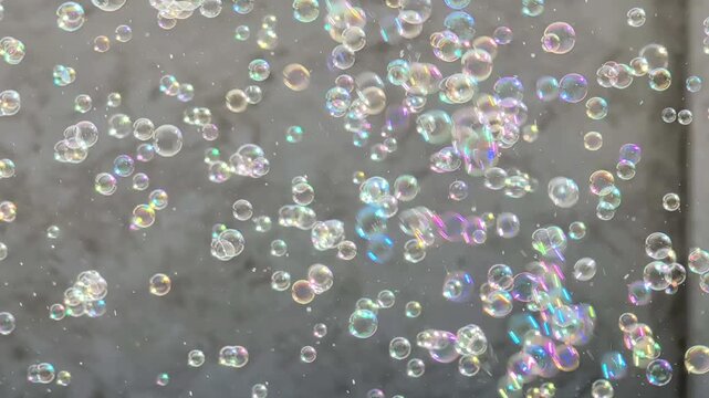 Colorful soap bubbles floating in the air against a blurred gray background, showcasing a dynamic progression of movement and light reflections in each frame