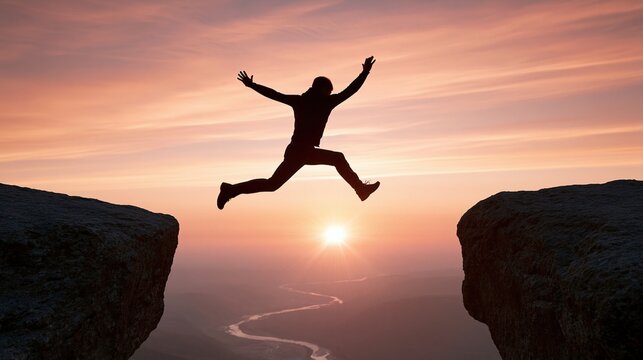 Silhouette of a person jumping joyfully between two cliffs against a vibrant sunset sky over a winding river valley