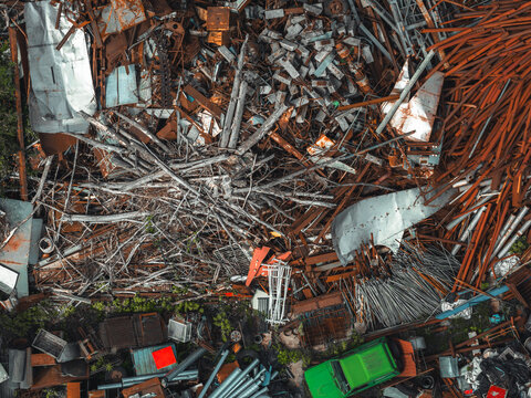 Aerial view of a metal recycling yard featuring piles of rusted scrap metal, discarded pipes, metal sheets, and a green vehicle in Poland.