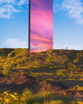 Surreal reflective monolith pillar on a grassy hill reflecting a pink sunset sky