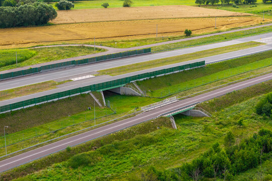 Aerial view of a wildlife green bridge and underpass spanning a highway, surrounded by lush green vegetation and agricultural fields in Poland.