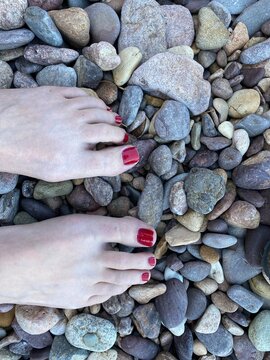 Bare Feet with Red Nail Polish Standing on Pebble Beach
