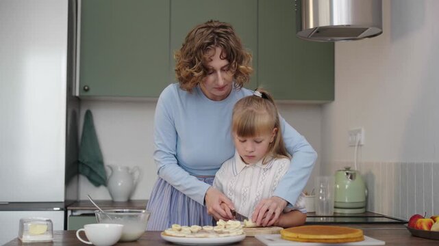 Mother and daughter bake layered cake together in cozy sunlit kitchen, 25 fps