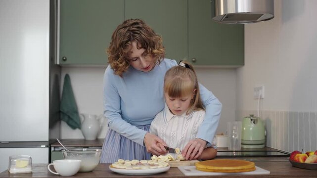 Mother and daughter bake layered cake together in cozy sunlit kitchen, 25 fps