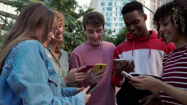 Group of diverse teenagers using smartphones together outdoors