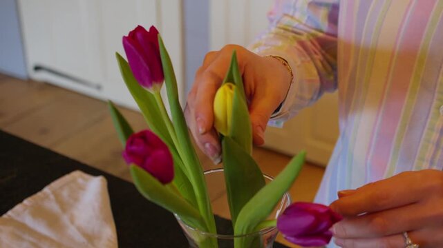 A florist places a single yellow tulip in a clear vase with several other pink tulips. The other flowers are then moved to compliment it.