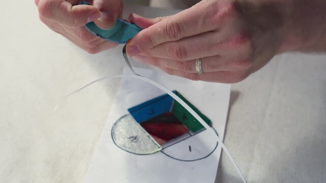 A married man uses his fingers to gently apply copper tape to a small piece of blue stained glass during an art class.