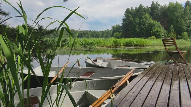 metal rowboats with wooden oars moored at wooden pier on calm river. peaceful summer scene with boats docked. concept of quiet vacation and nature tourism in rural landscape.