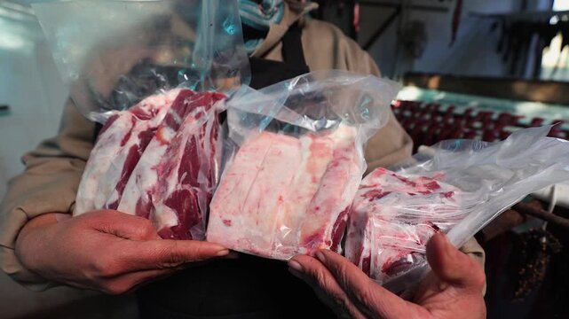 Butcher in apron holds several cuts of red meat in shrink wrap plastic
