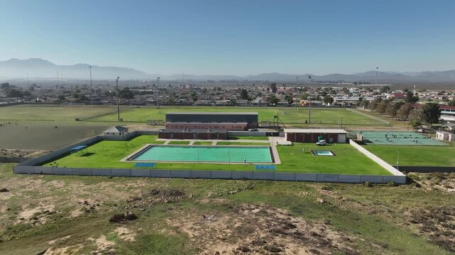 Low aerial circles large empty swimming pool on edge of mtn town